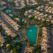 Aerial landscape of the Meadows and Emirates Hills neighborhoods in Dubai, UAE, showcasing luxury villas, lush green spaces, and serene lakes in an upscale residential community.
