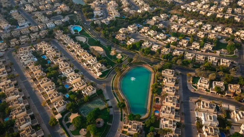 Aerial landscape of the Meadows and Emirates Hills neighborhoods in Dubai, UAE, showcasing luxury villas, lush green spaces, and serene lakes in an upscale residential community.