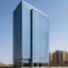 A modern commercial tower in Dubai’s International City, showcasing sleek all-glass architecture and a landscaped entrance plaza under clear skies.