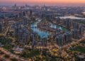 Aerial view of a Dubai master-planned mega project district with residential towers, lagoons and green public spaces at dusk