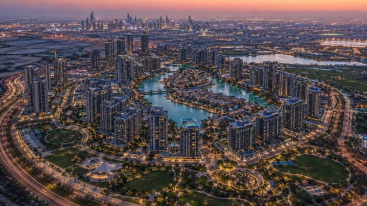 Aerial view of a Dubai master-planned mega project district with residential towers, lagoons and green public spaces at dusk