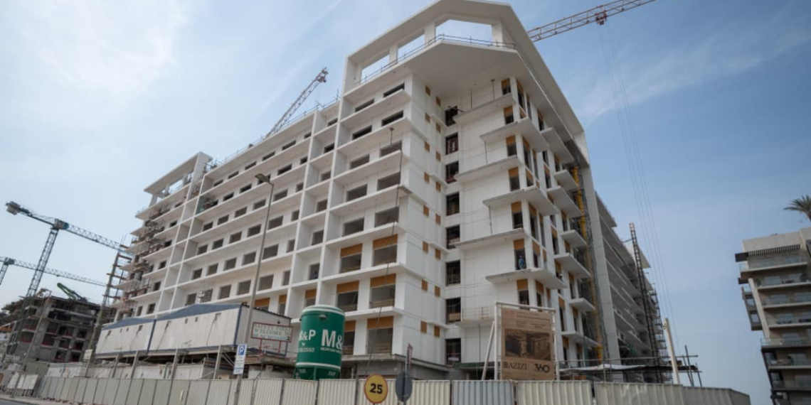 Azizi Beach Oasis II low-rise blocks under construction in Dubai Studio City, October 2026, with façade work still under way. Commission or request a current site photo from Azizi; avoid launch renders, which show a finished building the story says is not yet close.